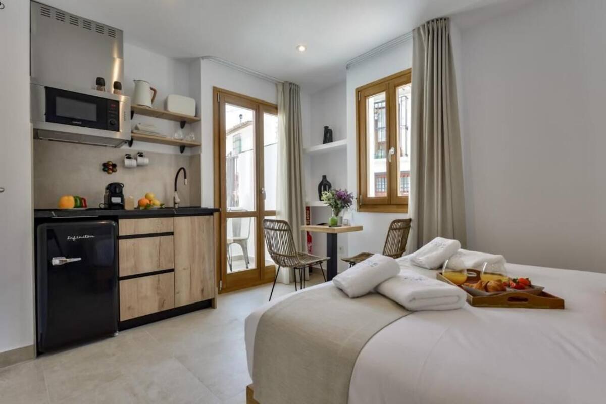 Une chambre d’hôtel compacte avec une kitchenette, un lit agrémenté d’un plateau de petit-déjeuner et une vue par la fenêtre.