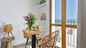 Un balcón con vista al mar, una mesa con un florero, sillas de mimbre y una lámpara.
