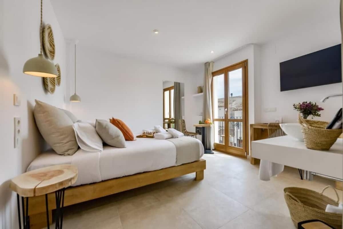 Une chambre moderne avec un lit, une table de chevet et une vue sur la ville grâce à de grandes fenêtres.