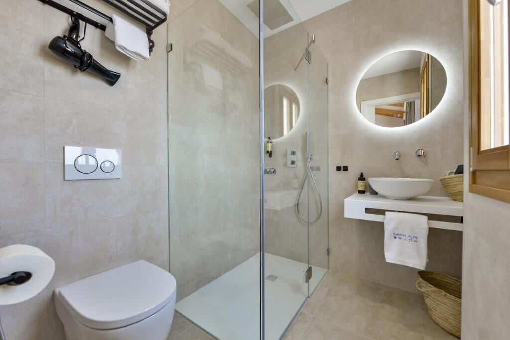 A modern bathroom with a glass-enclosed shower, a white toilet, a sink with a mirror, and a towel hanging on the wall.