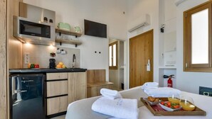 Habitación de hotel compacta con kitchenette, una cama con una bandeja de desayuno y una puerta de madera.