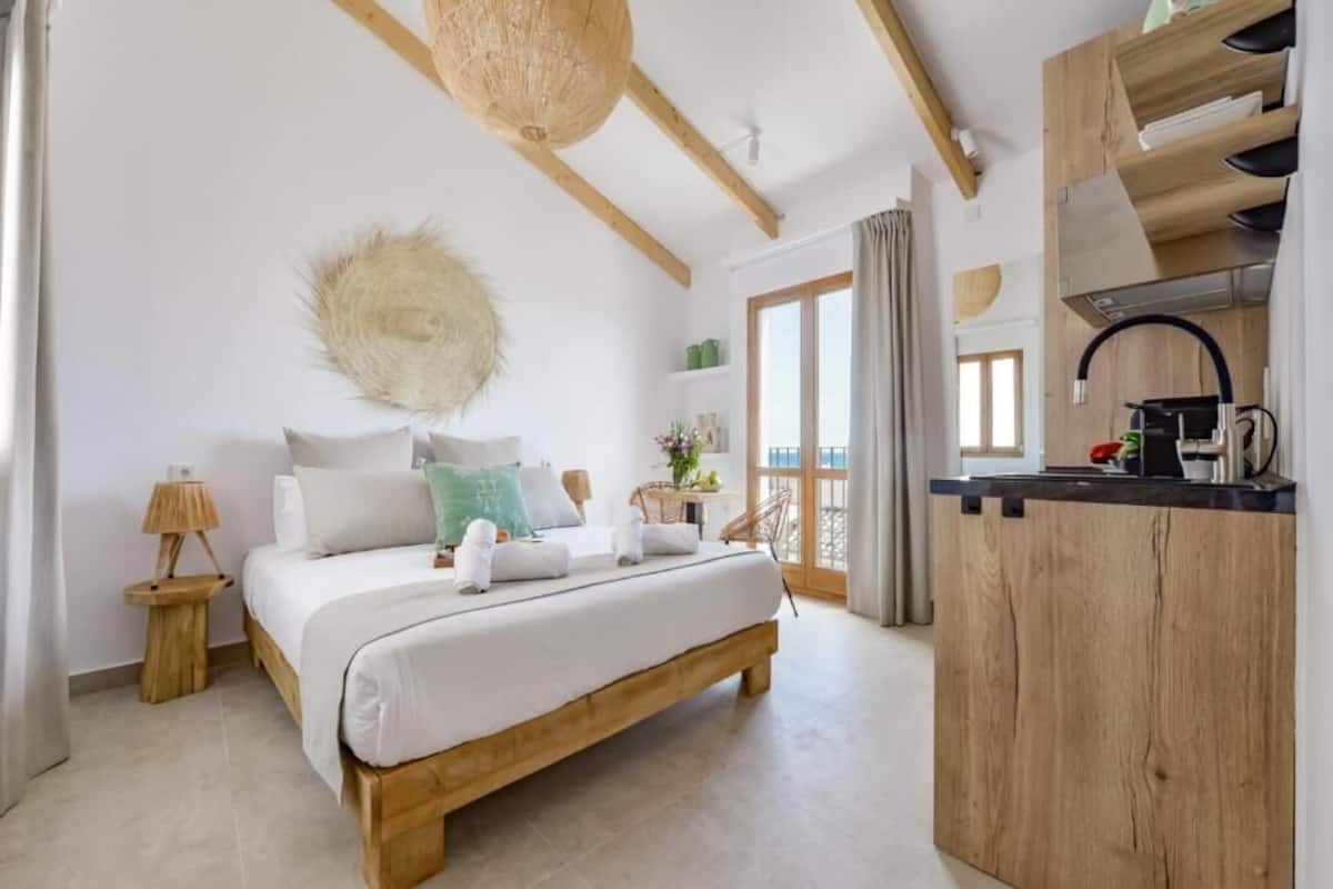 Une chambre avec un lit en bois, une petite table de chevet, un luminaire suspendu et une vue sur le balcon.