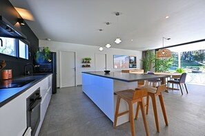 A modern kitchen with a central island, bar stools, and a dining area with a view. - Exceptional villa with Sainte-Victoire view (Aix-en-Provence) next to golf course (Peynier)