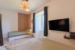 Une chambre à coucher avec un lit, un téléviseur, une petite table avec une lampe, une fenêtre avec des rideaux et un téléviseur fixé au mur.