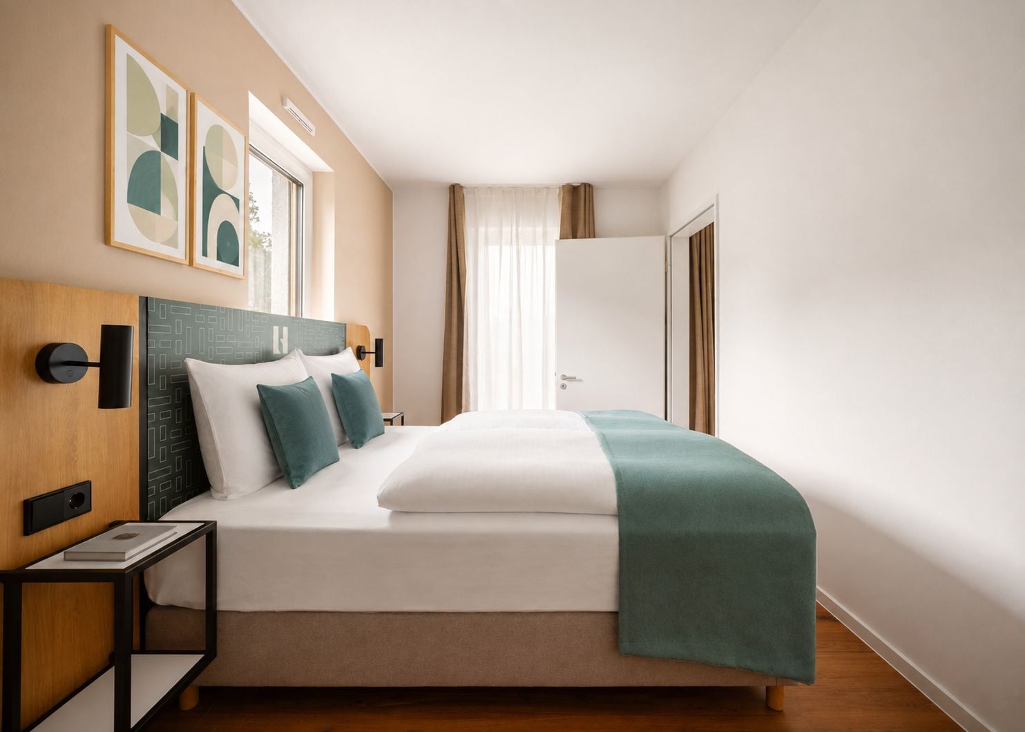Ein modernes Hotelzimmer mit einem großen Bett, einem Kopfteil mit geometrischen Mustern, einem Nachttisch mit einem Buch und abstrakter Kunst an der Wand.