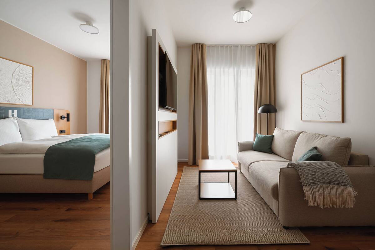 A modern hotel room with a bed, a sofa, a small table, and a TV.