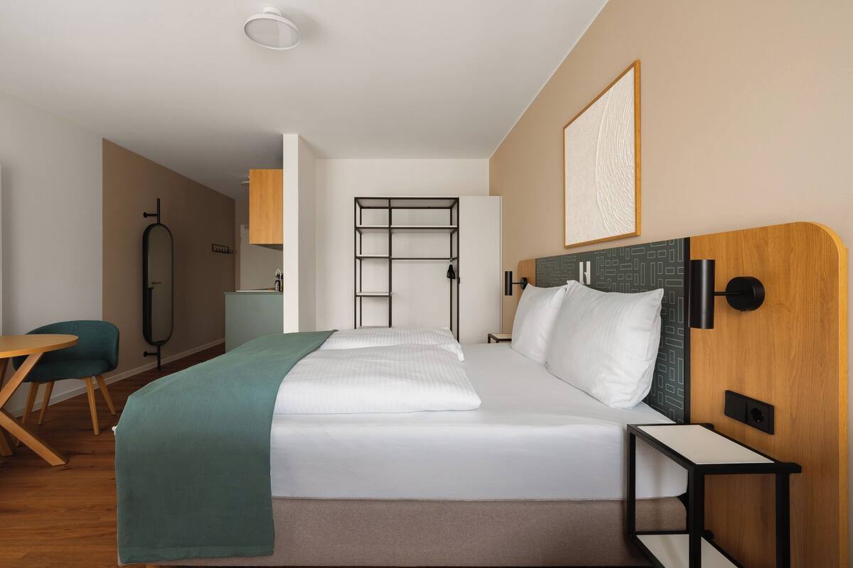 A hotel room with a bed, bedside table, desk, chair, and a TV.
