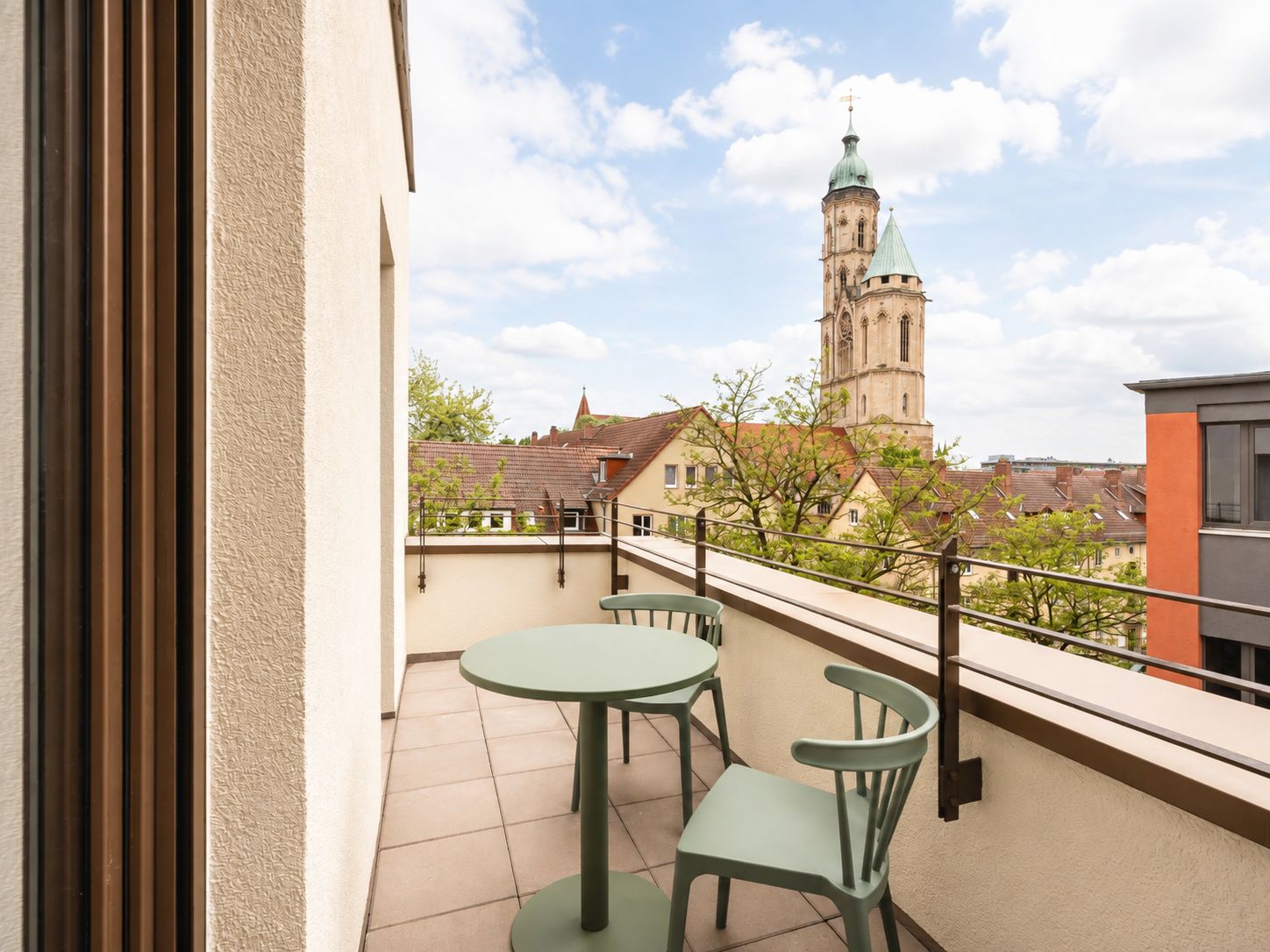 A balcony with a table and chairs, overlooking a historic building with a tower.
