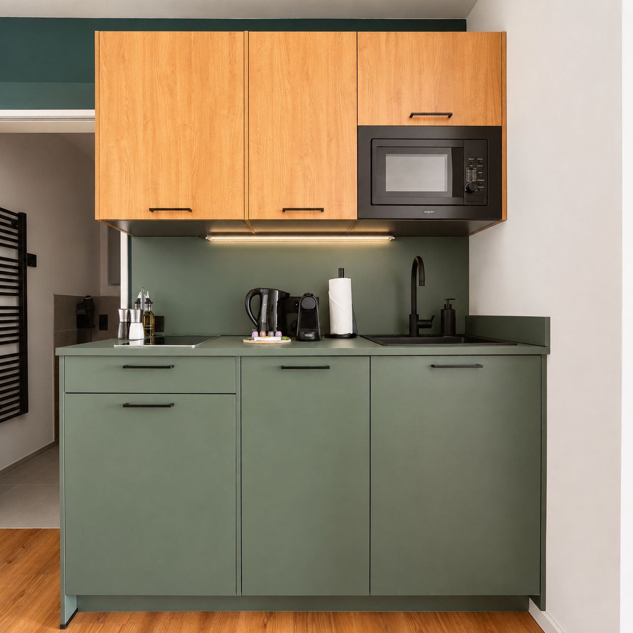 A kitchen with green cabinets, a microwave, a coffee maker, and a sink.