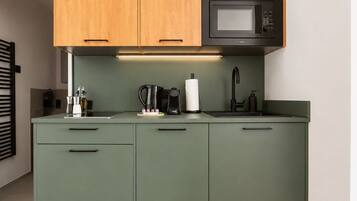 A kitchen with green cabinets, a microwave, a coffee maker, and a sink.