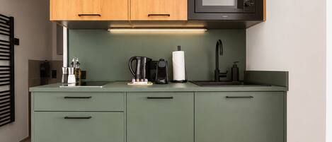 Cozinha com armários verdes, micro-ondas, cafeteira e pia.