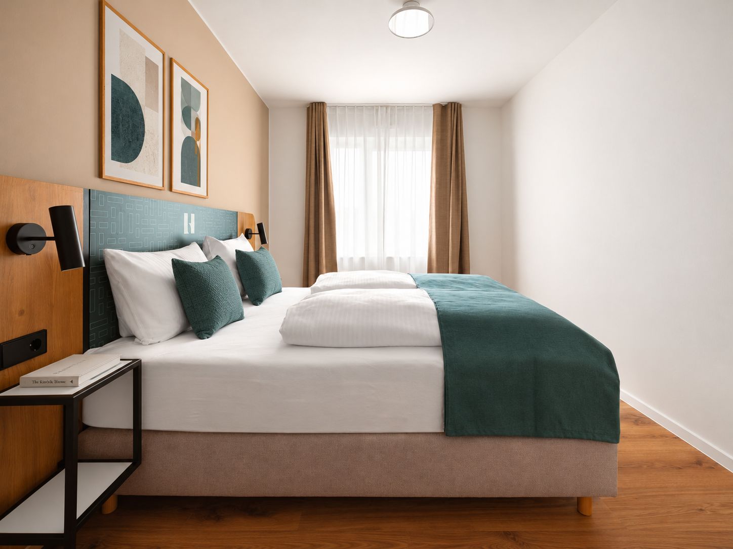 Una habitación de hotel moderna con una cama grande, una mesita de noche, una lámpara de pared y dos obras de arte abstractas enmarcadas.