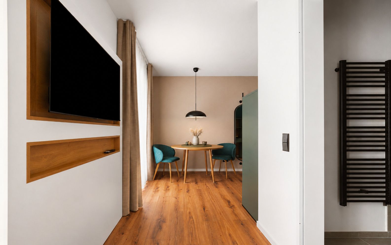 A modern interior with a wooden floor, a dining area with two chairs, a table, and a TV mounted on the wall.
