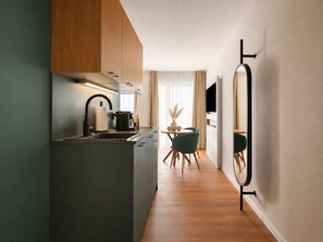 A modern kitchen with a central island, a dining area with a round table and chairs, and a large mirror on the wall. - Limehome Braunschweig Kaiserstraße  (Braunschweig)