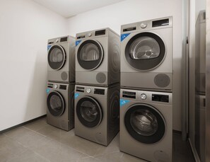 A row of stacked front-loading washing machines in a room with white walls and tiled flooring.