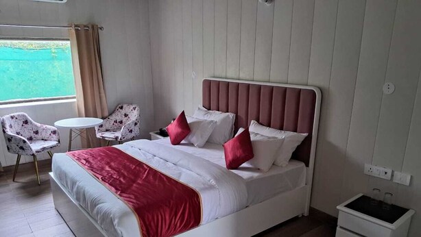A bedroom with a bed, bedside tables, a chair, and a view of the outdoors. - Vishalgarh Farms  (Gurugram)