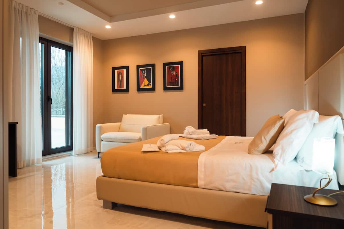 A modern hotel room with a large bed, a sitting area, and a door leading to a balcony.