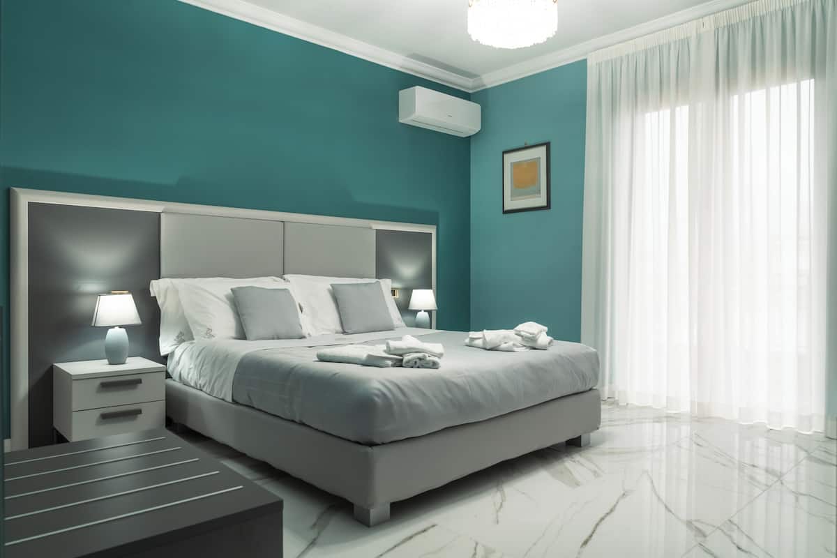 A modern bedroom with a large bed, bedside tables, a nightstand, and a ceiling-mounted air conditioner.