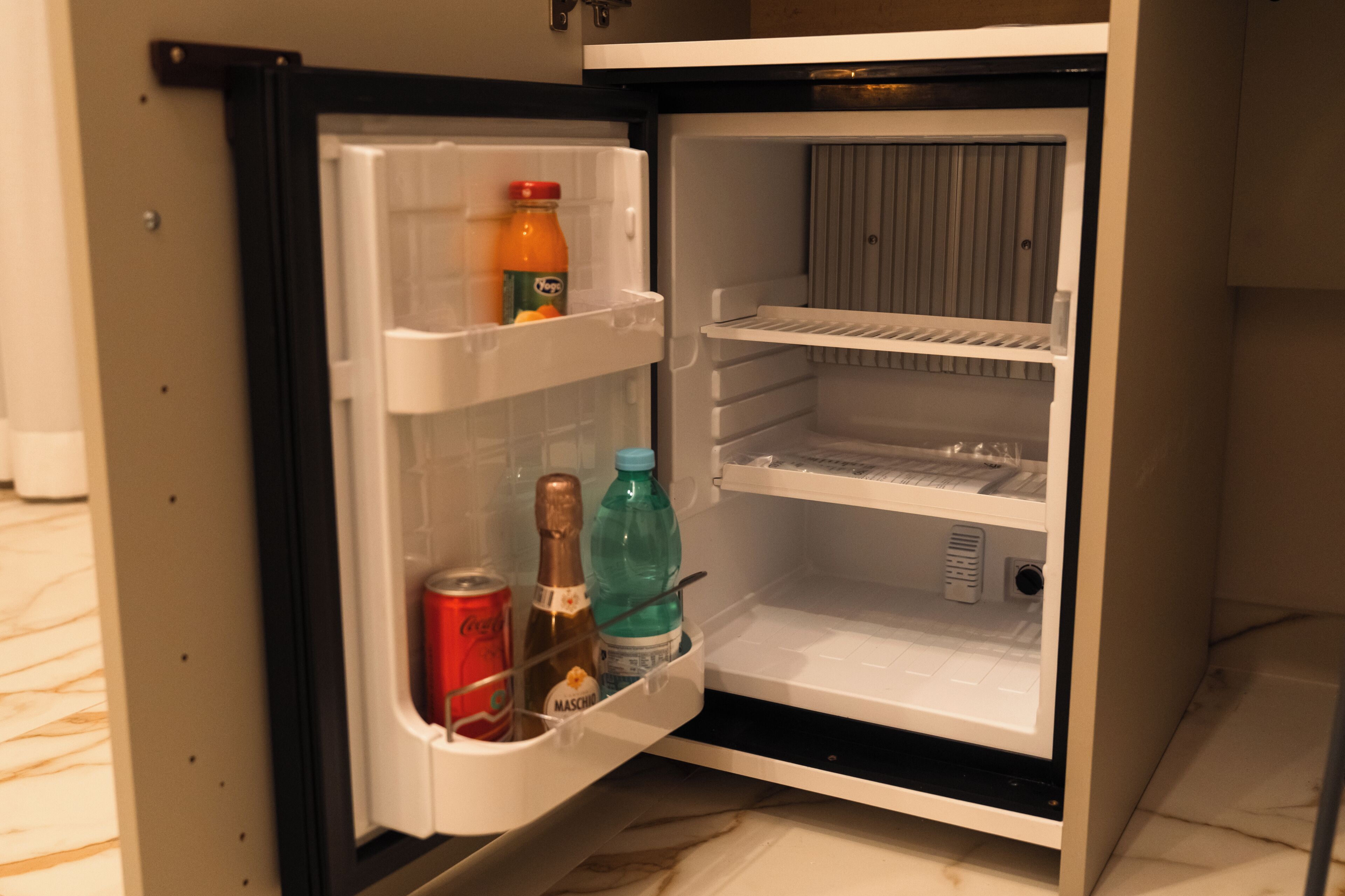 Ein offener Kühlschrank mit Orangensaft, einer Cola und einer Wasserflasche.