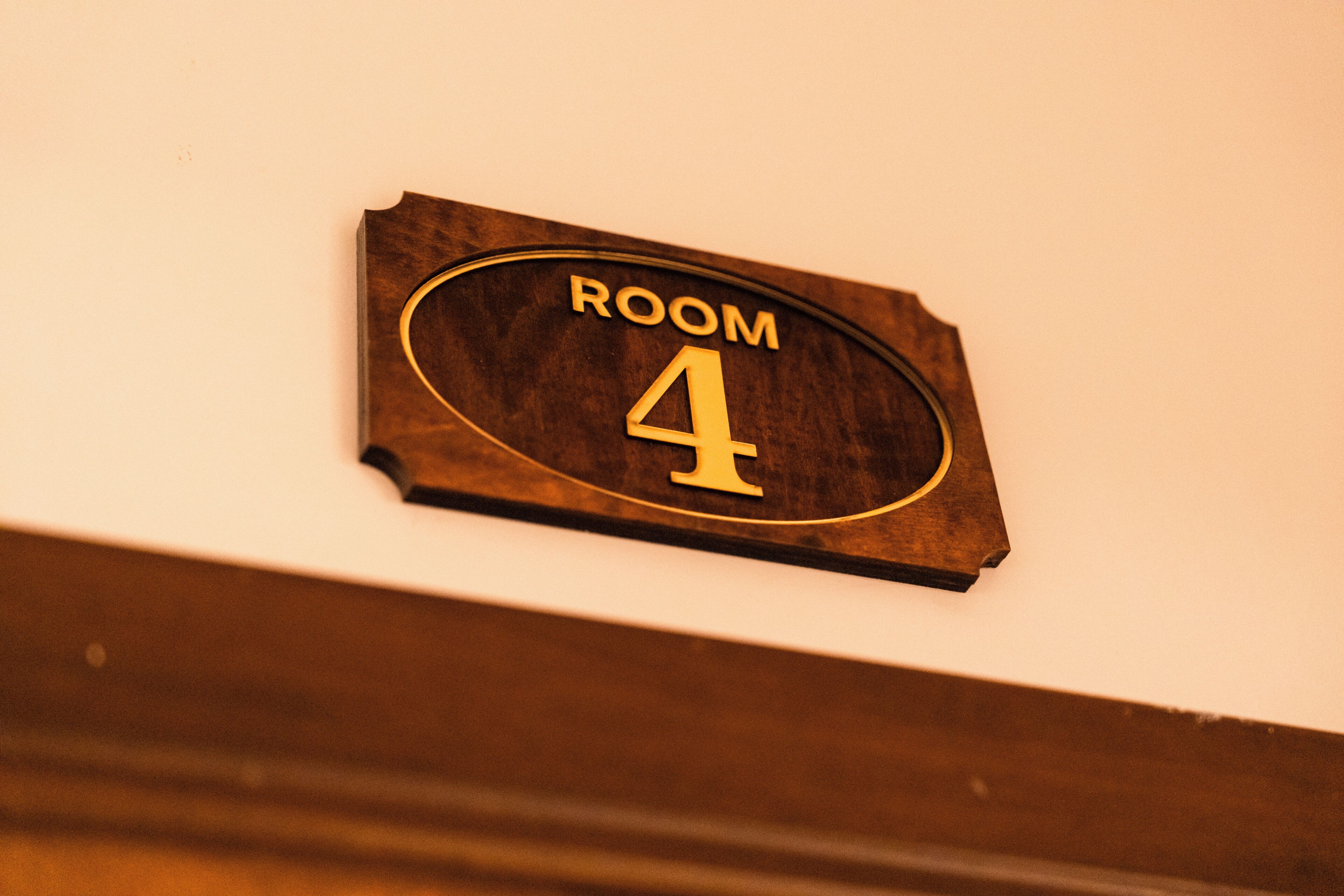 A wooden sign with the text 'ROOM 4' on a white wall.