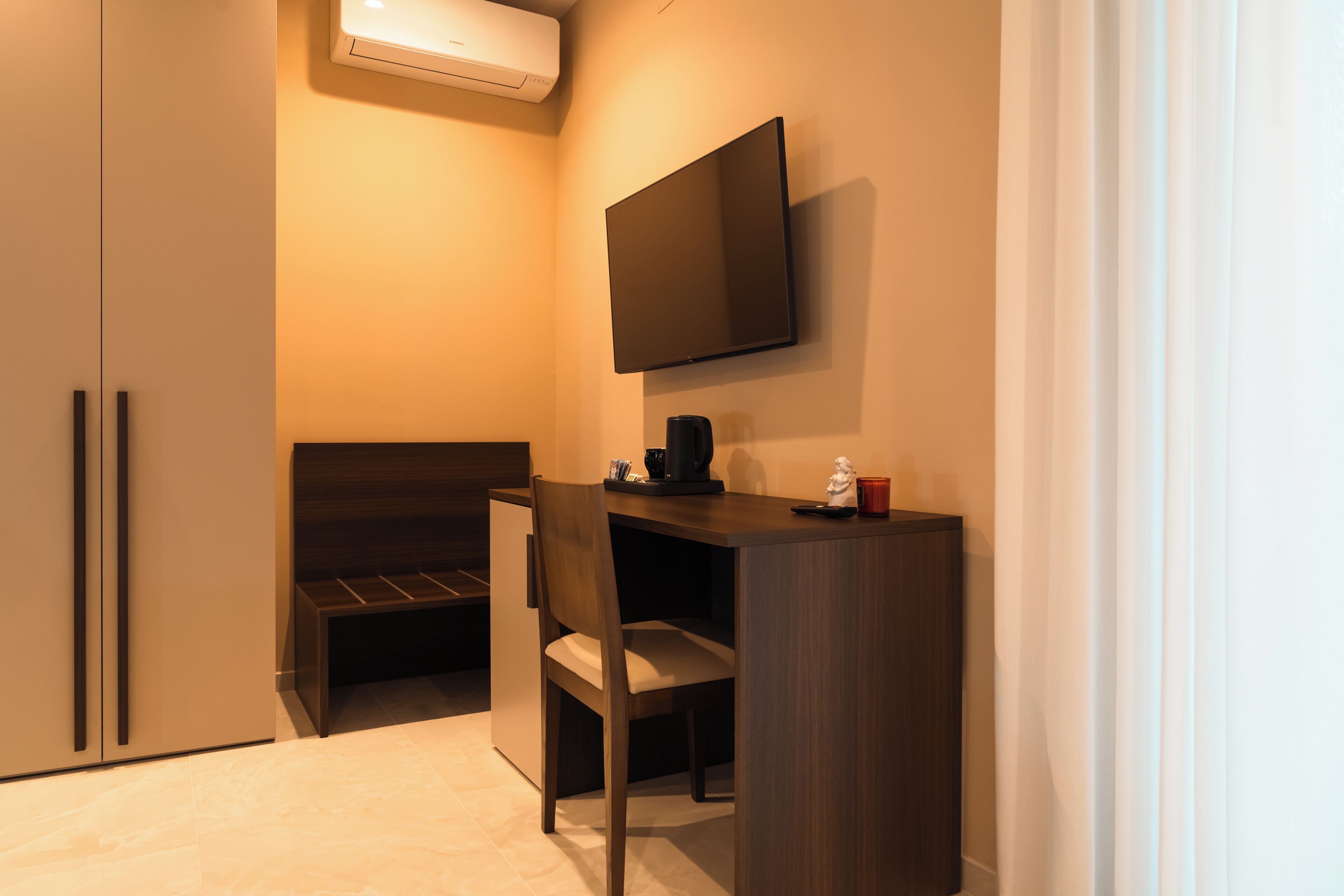 A compact room with a bed, a desk, a chair, a flat-screen TV, and a small table with a coffee maker.