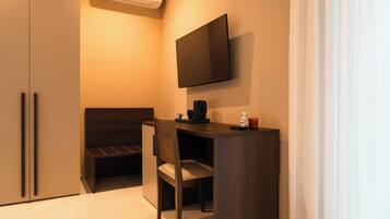 A compact room with a bed, a desk, a chair, a flat-screen TV, and a small table with a coffee maker.