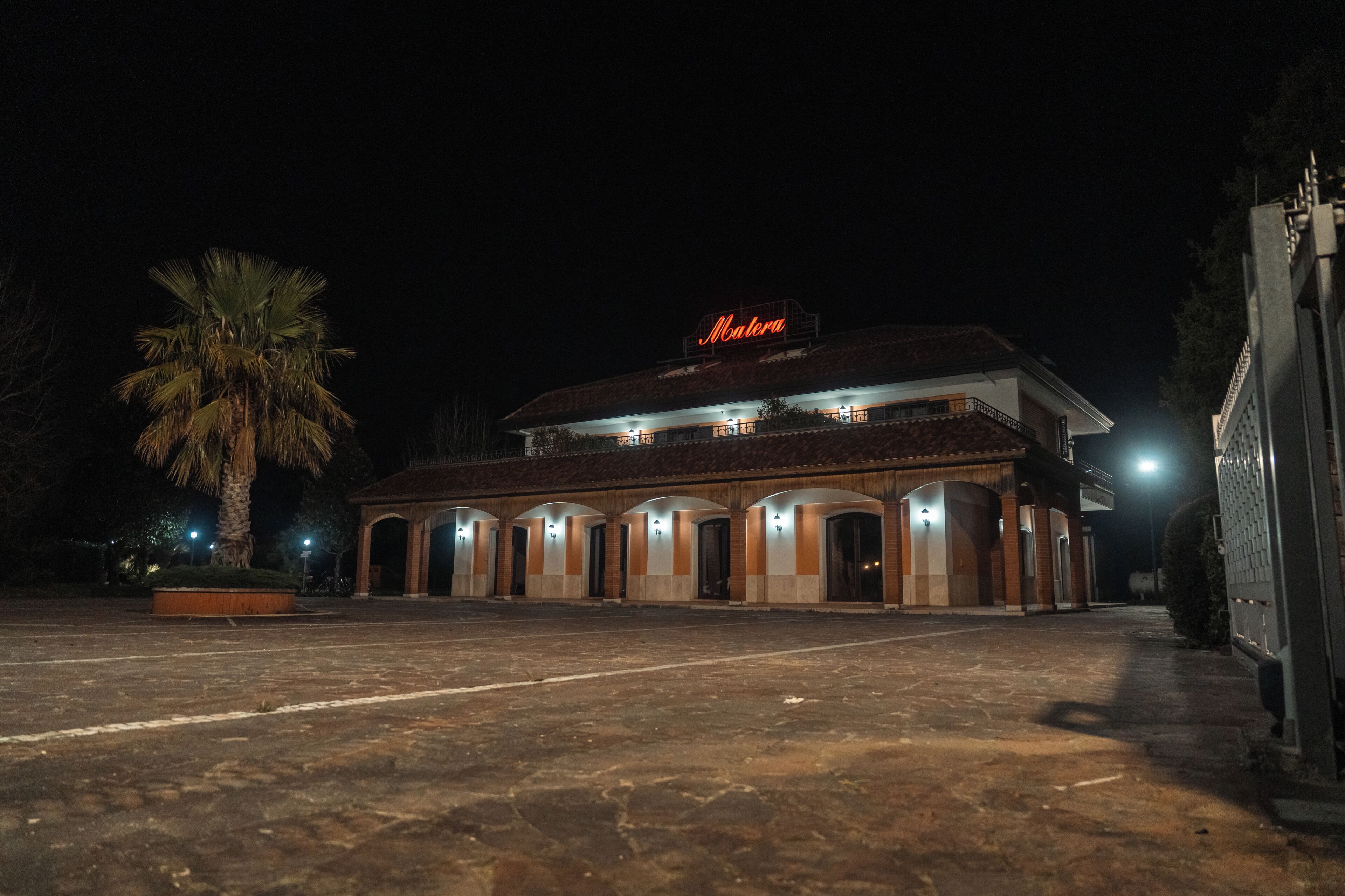 A building with a sign 'Matera' at night, featuring a central courtyard and multiple arched doorways.