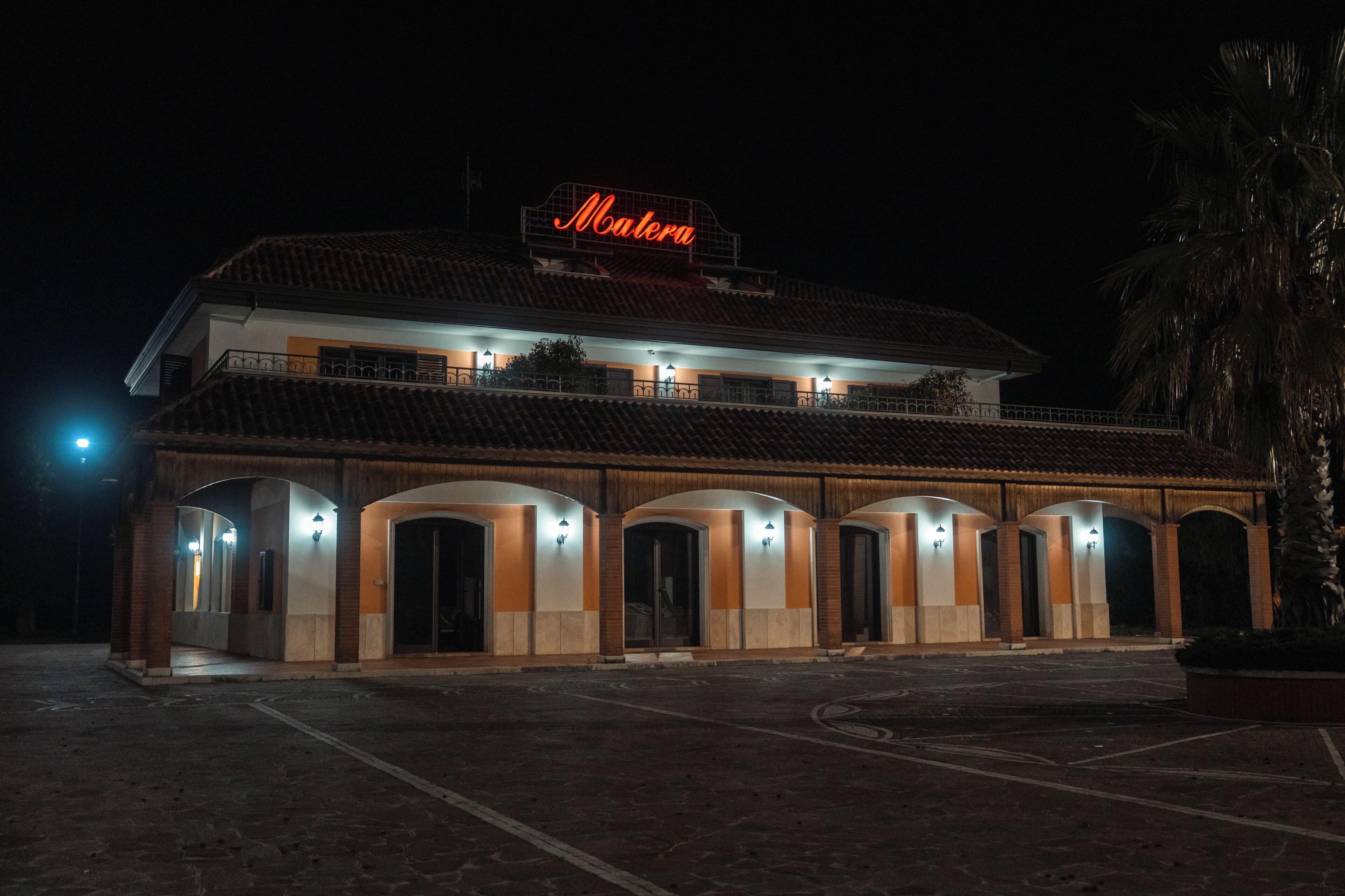 A hotel with a sign reading 'Matera' at the top, multiple arches, and a paved entrance area.