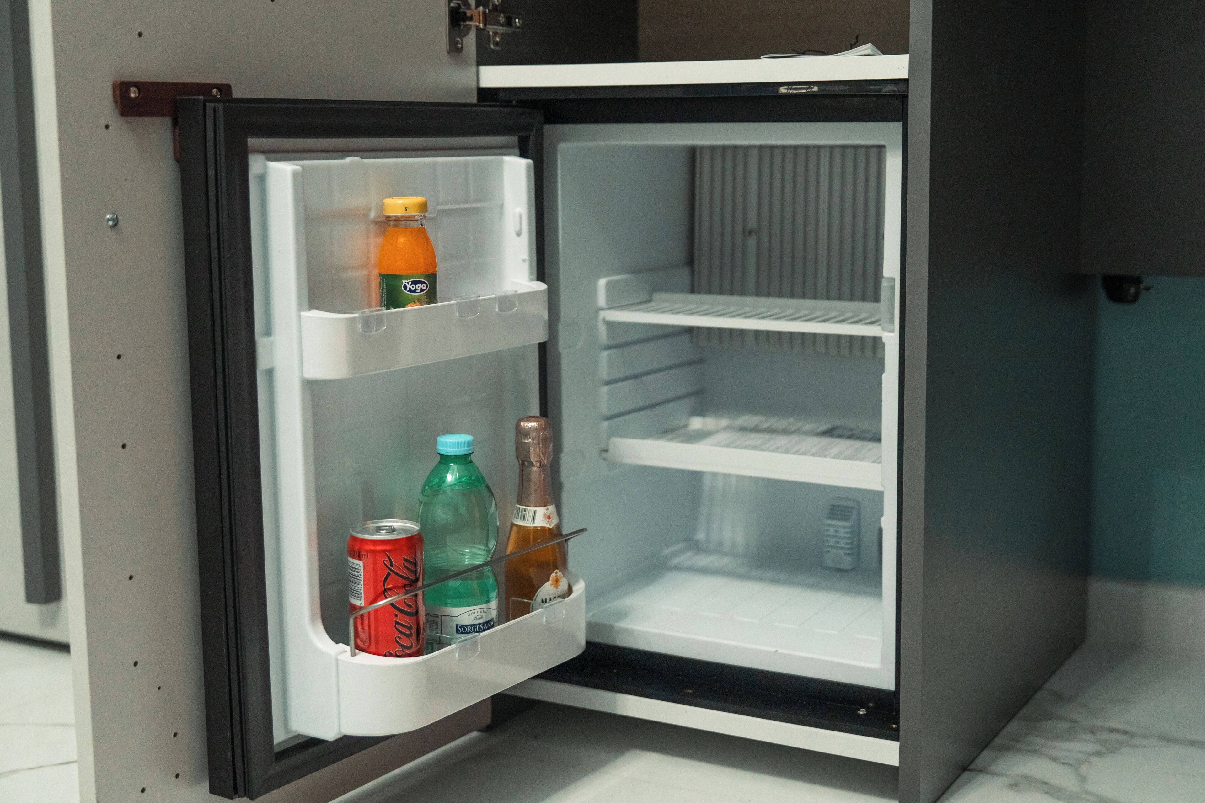 Un refrigerador abierto con un dispensador de bebidas, una botella y una lata.