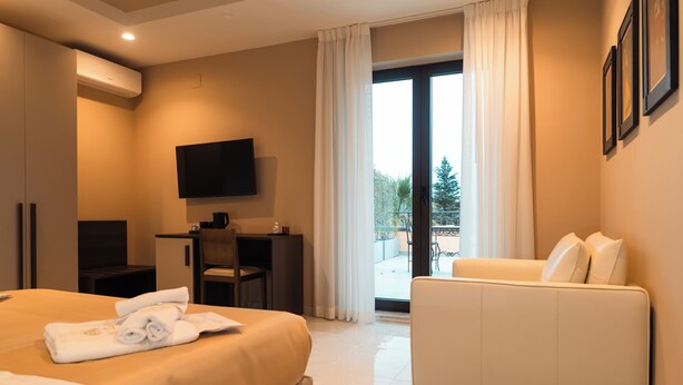 Habitación de hotel con cama, escritorio, televisor, sofá y balcón con vistas.