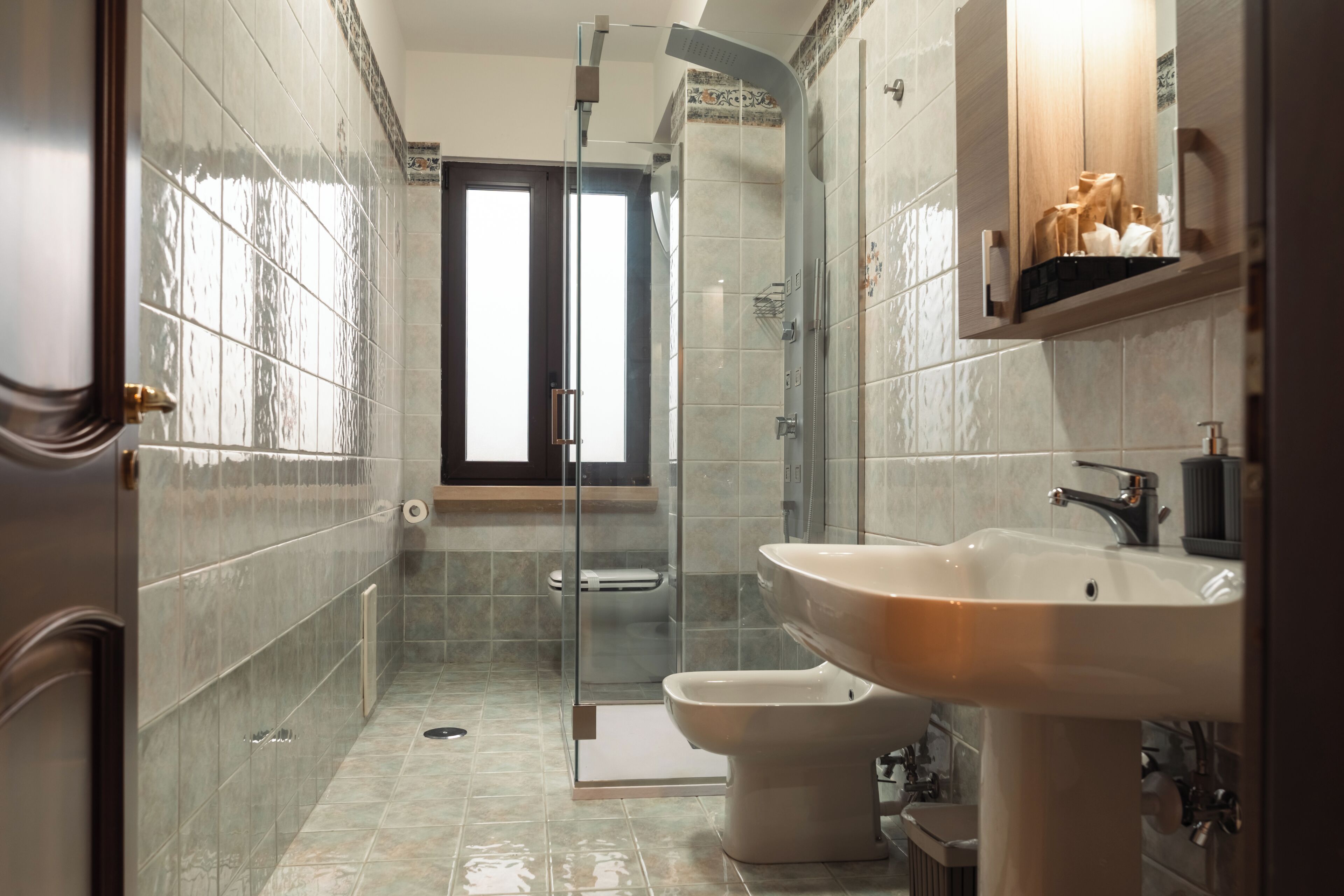 Un baño con cabina de ducha de vidrio, inodoro, lavabo y ventana que proporciona luz natural.