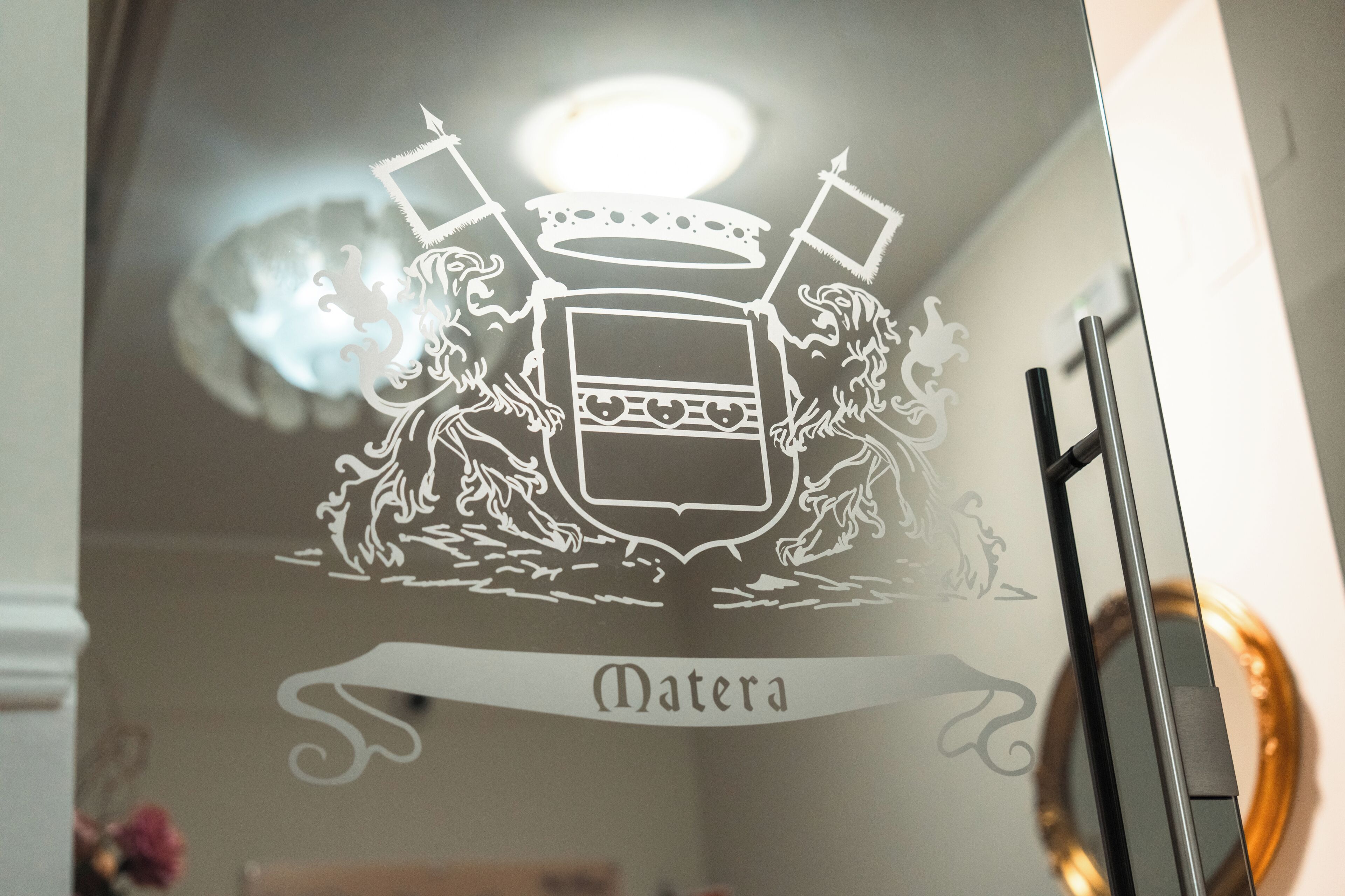 Una ventana de cristal con un escudo de armas y la palabra 'Matera' debajo.