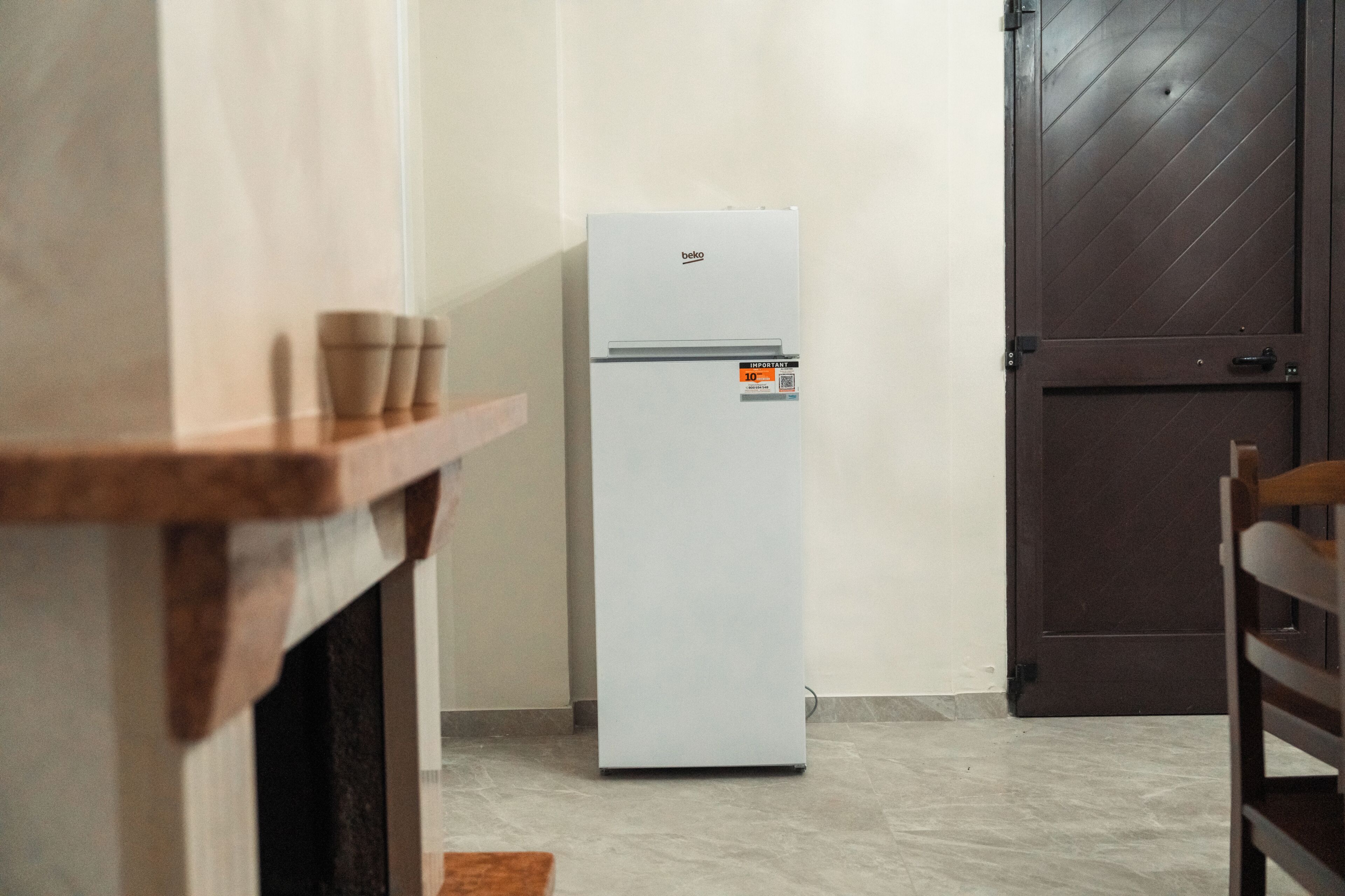Una cocina con un refrigerador blanco, una mesa de madera y una puerta de madera oscura.
