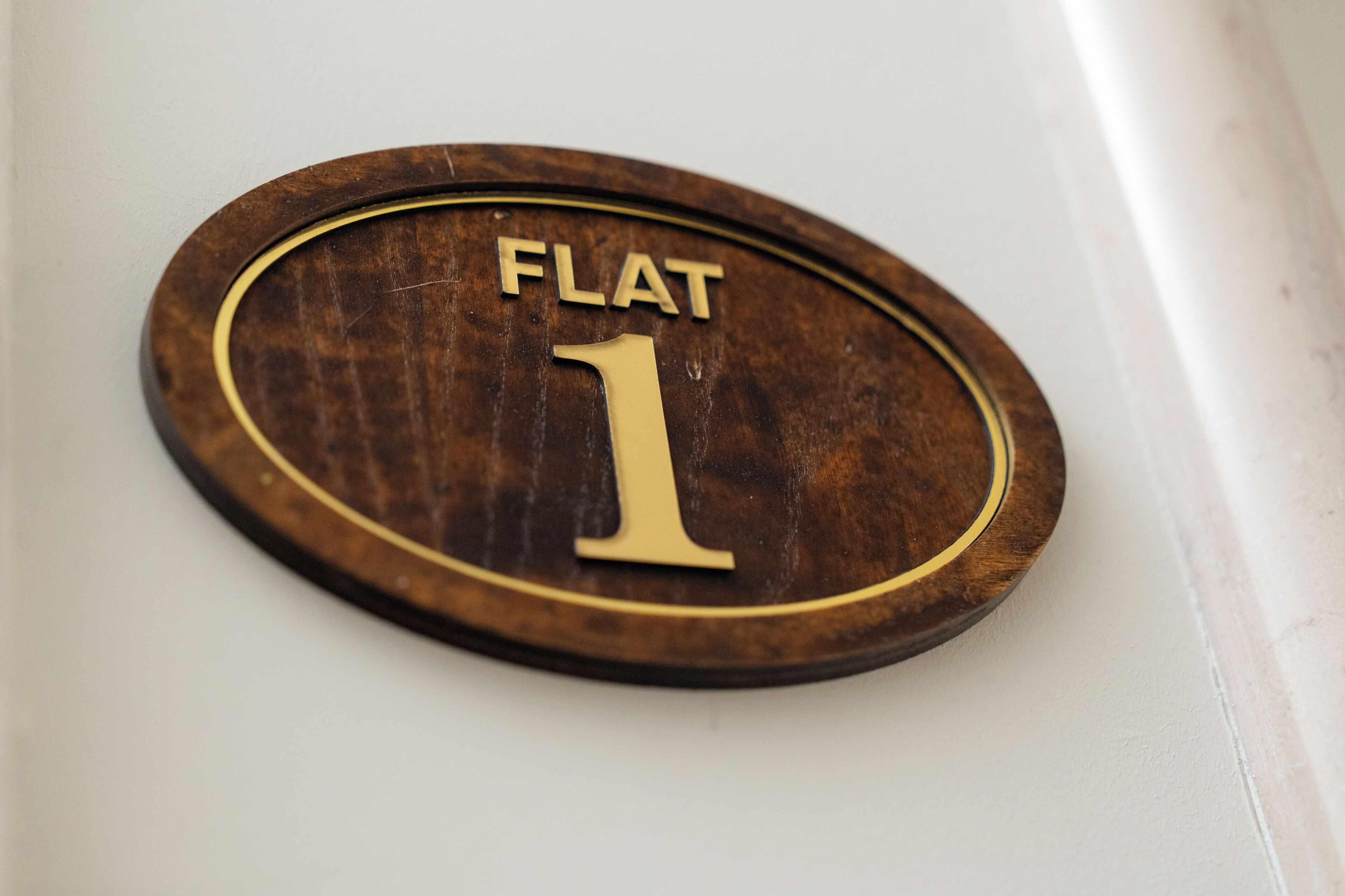 A wooden plaque with the text 'FLAT 1' on a white wall.