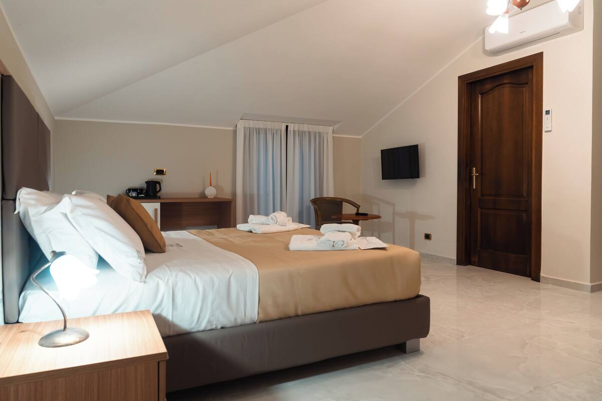 A hotel room with a bed, bedside table, lamp, TV, and a door.