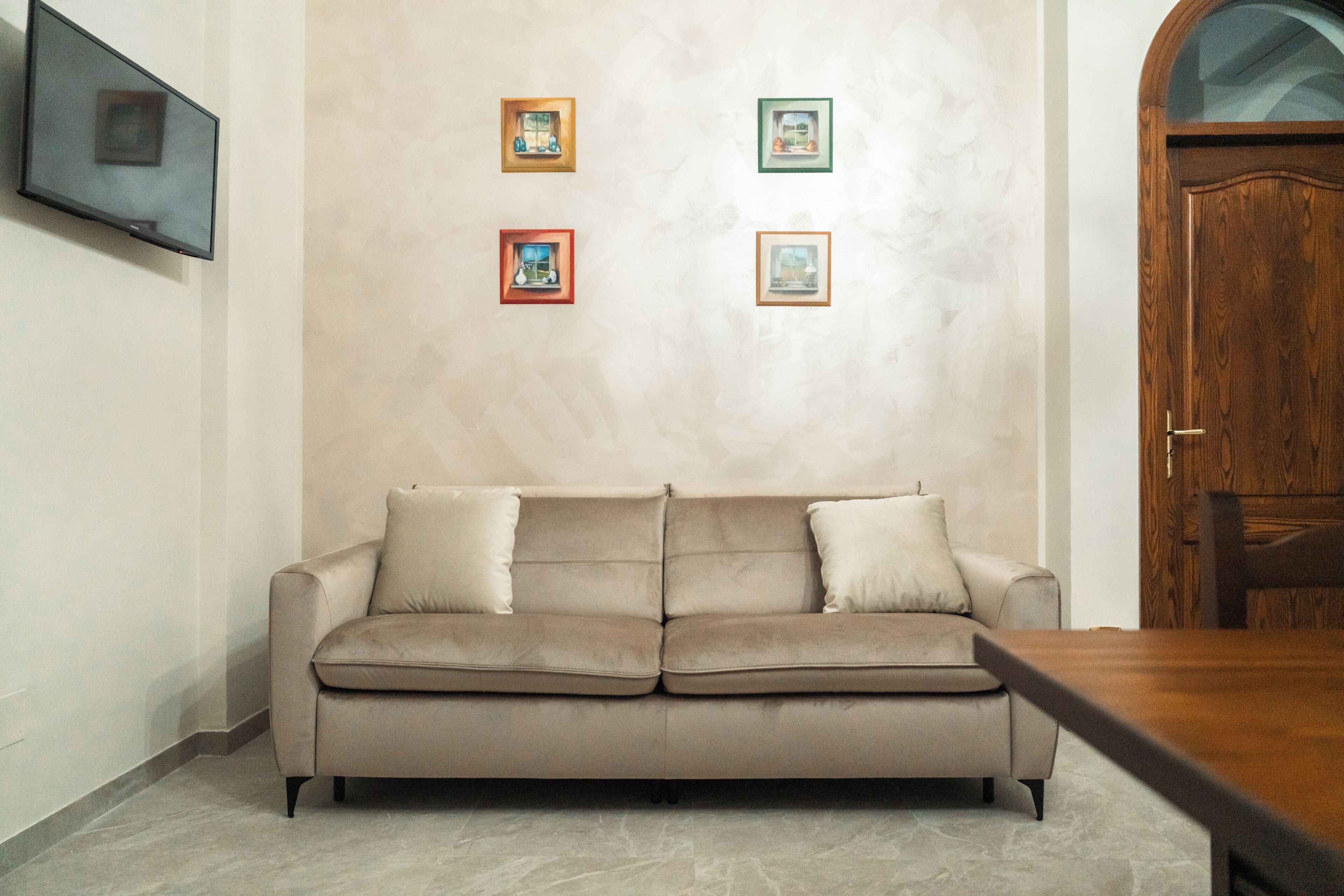 Un canapé beige avec deux coussins, une table à manger en bois et quatre tableaux encadrés accrochés au mur.