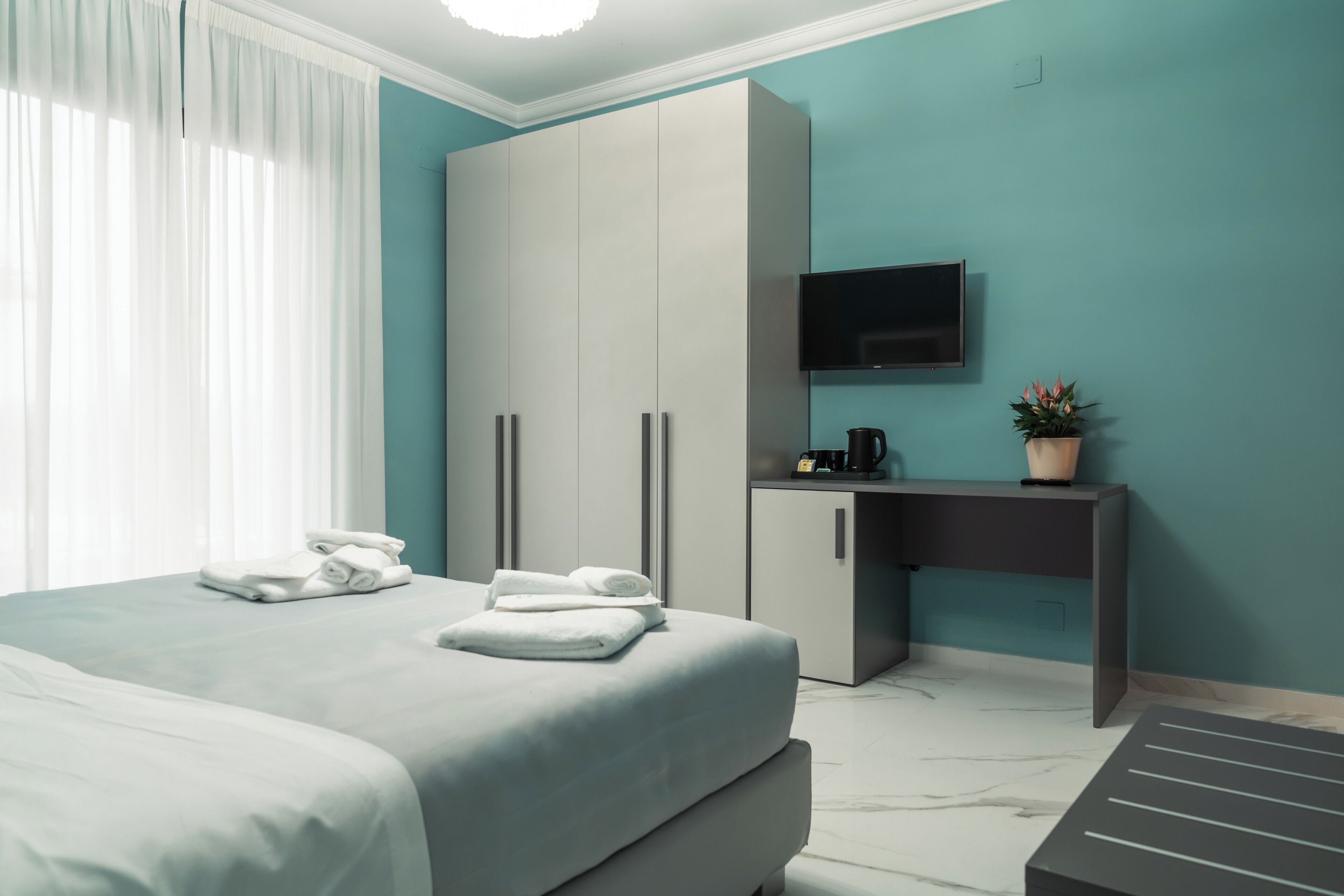 Una habitación de hotel con cama, escritorio, televisión y una planta en maceta.