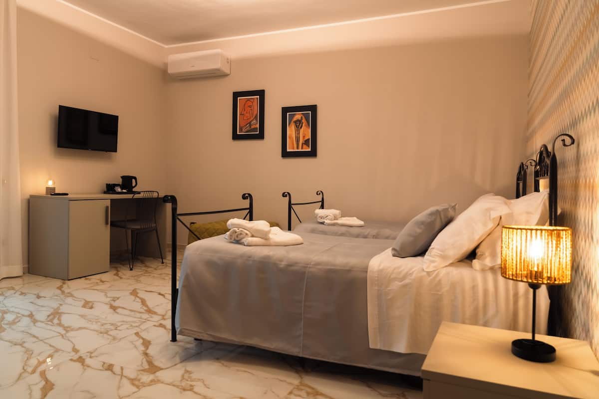 A hotel room with a bed, bedside table, lamp, desk, chair, TV, and artwork on the wall.
