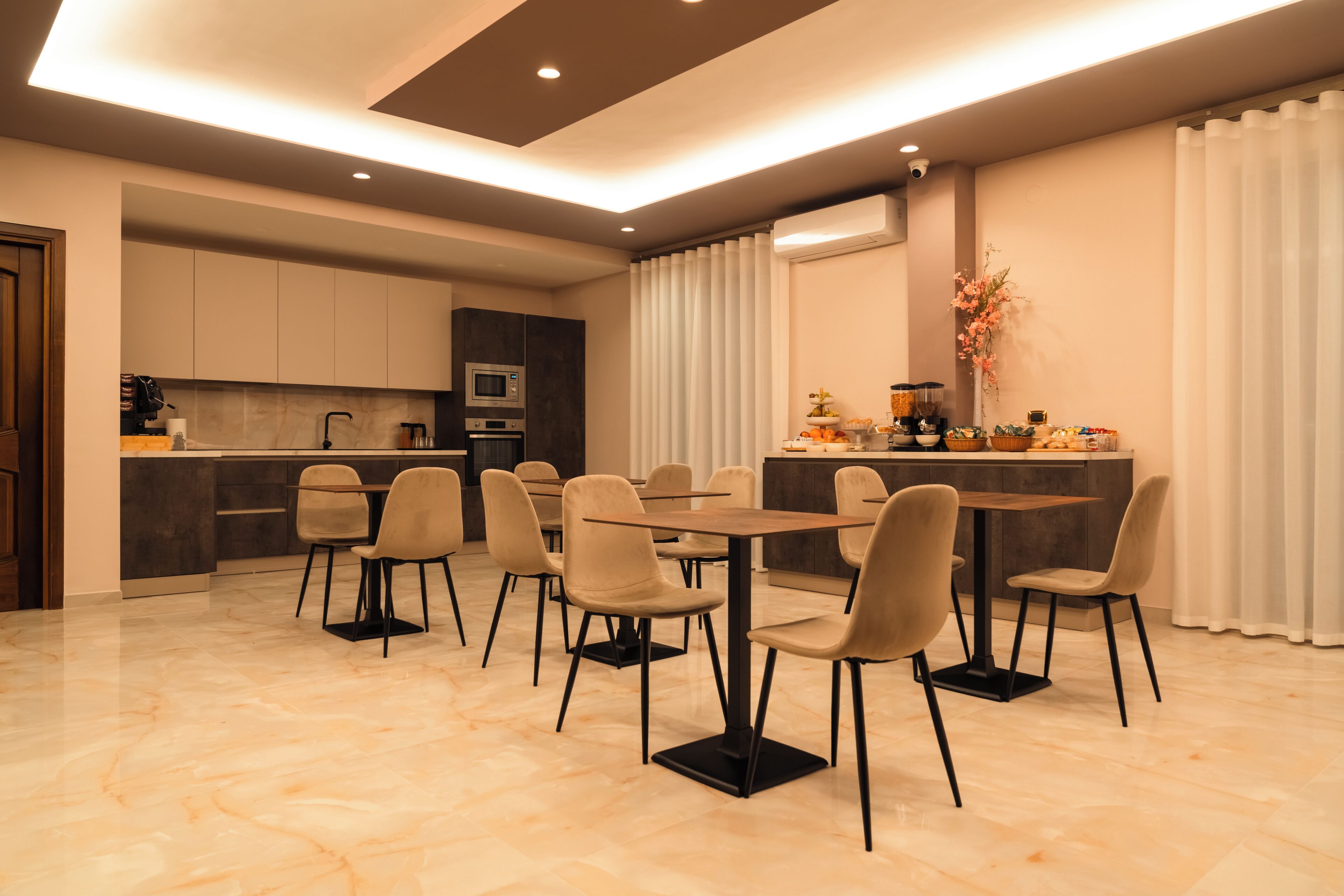 Een moderne eetruimte met een centrale tafel en stoelen, een keuken op de achtergrond en een decoratieve plant aan de rechterkant.