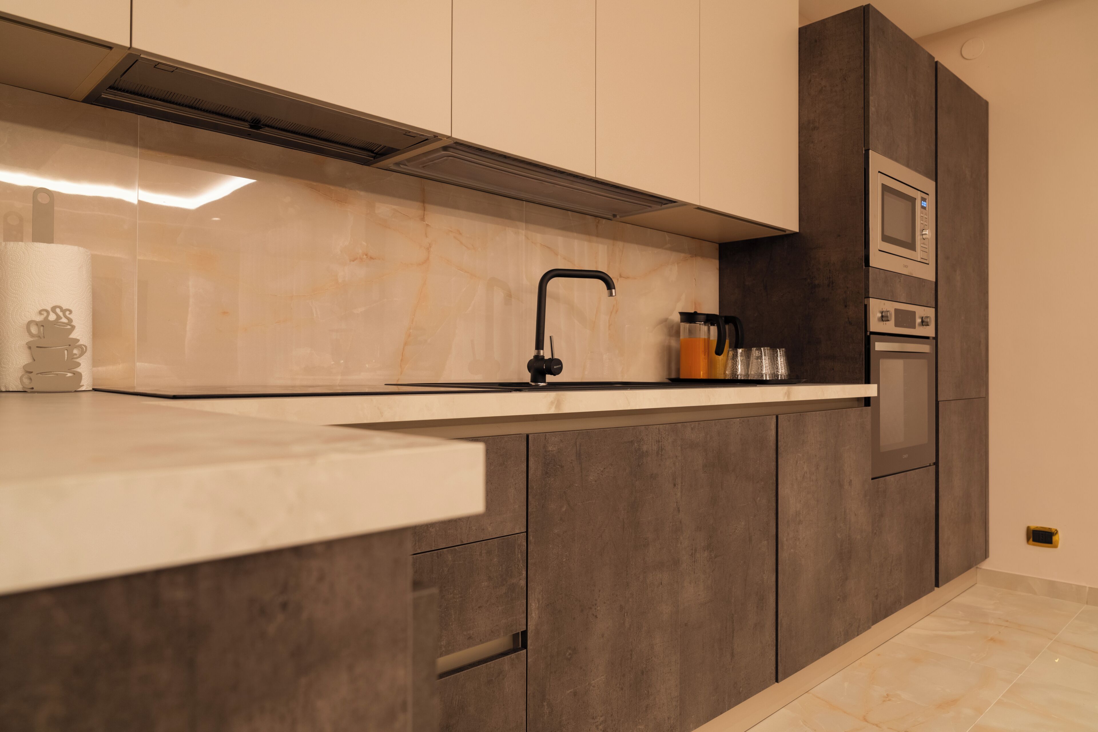 A modern kitchen with a marble countertop, dark cabinetry, and built-in appliances.