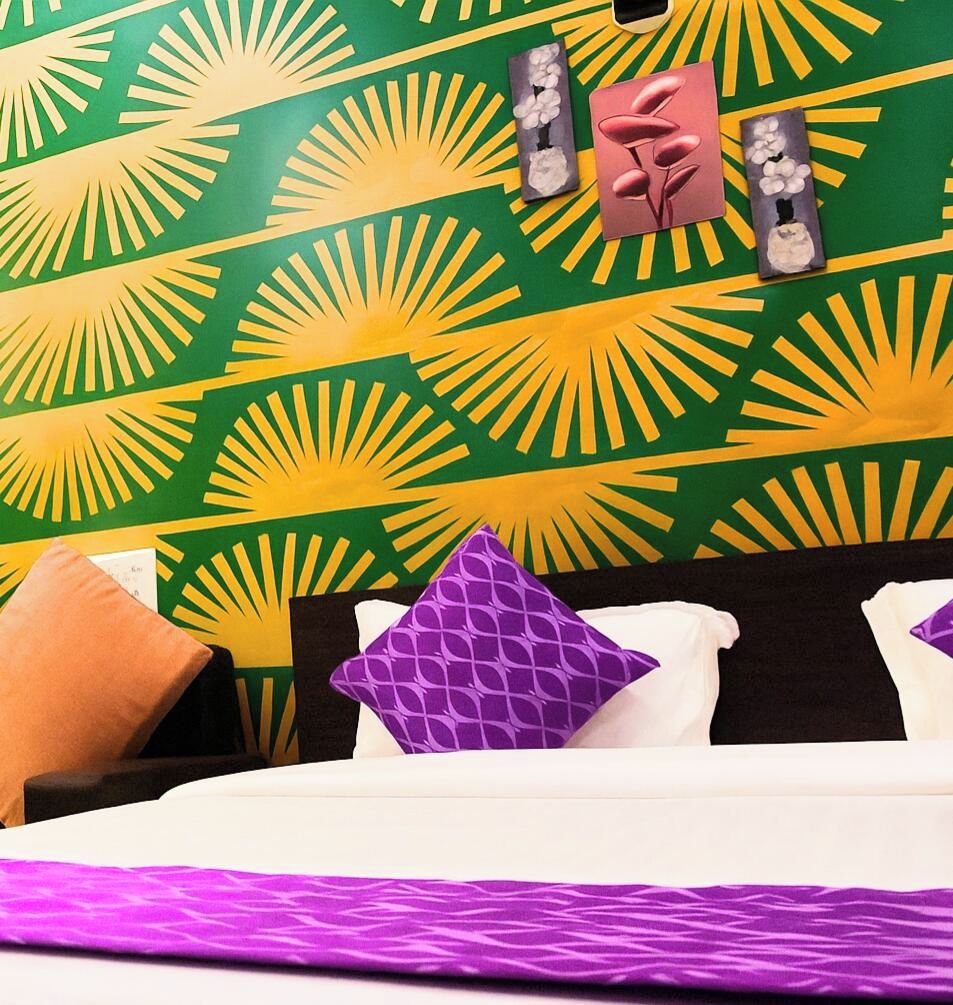 Una cama con una colcha blanca y morada estampada, un almohadón marrón y un cabecero negro.