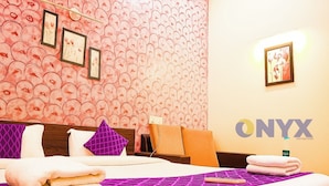 Een hotelkamer met behang met een patroon, een bed met meerdere kussens, een nachtkastje met een lamp en een ingelijst schilderij aan de muur.