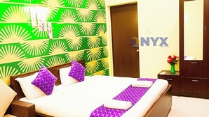 Een hotelkamer met een bed, nachtkastjes, een dressoir, een spiegel en een groene, patroonbehangen muur.