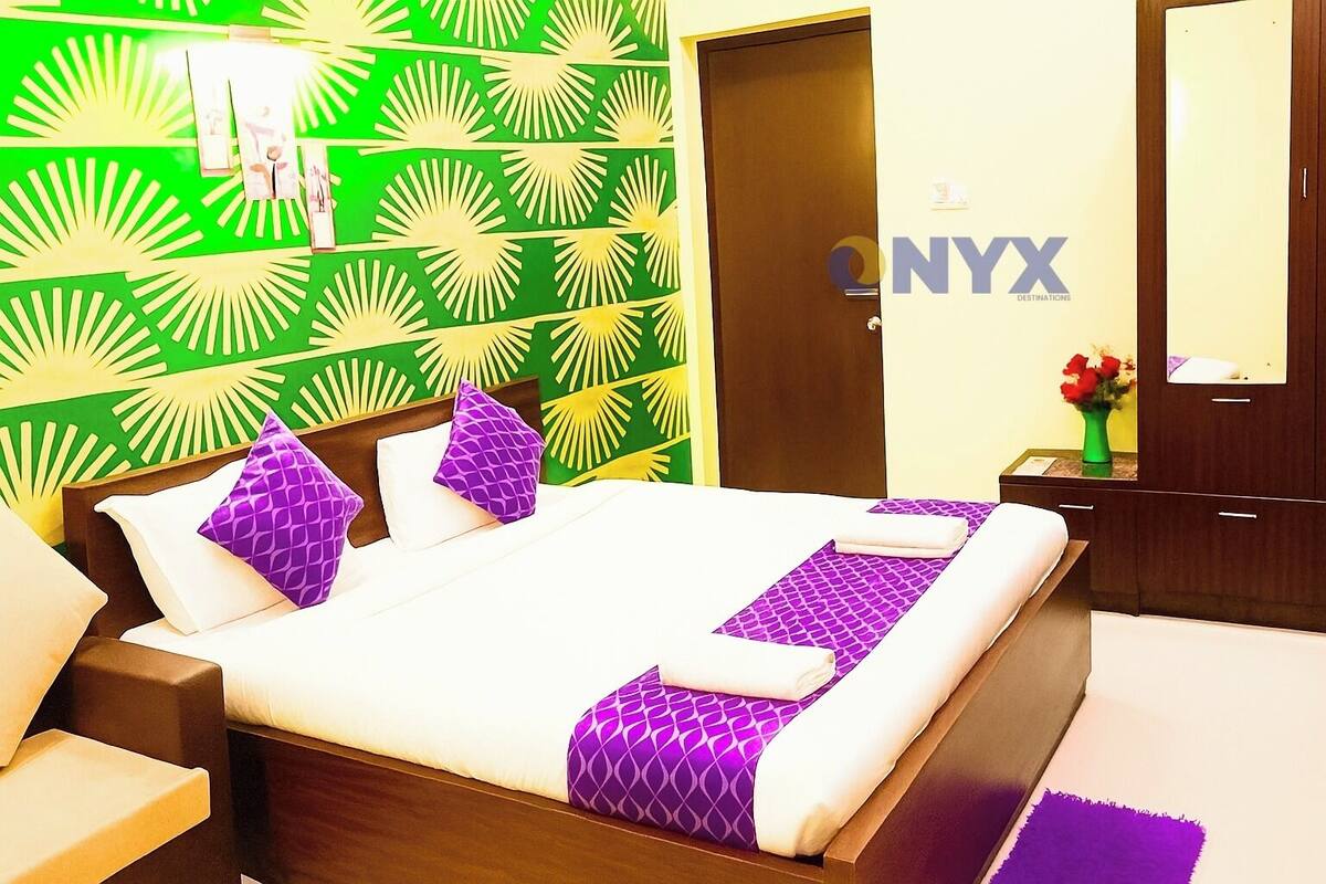 Una habitación de hotel con cama, mesitas de noche, cómoda, espejo y pared con diseño verde.
