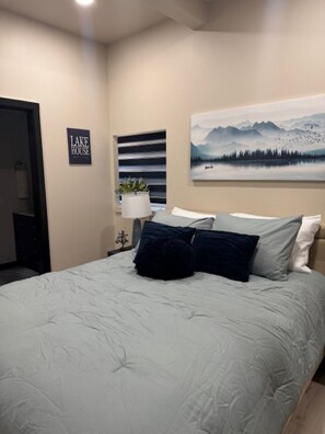 Una camera da letto con un letto, un quadro raffigurante montagne, un cartello con la scritta 'LAKE HOUSE' e una pianta in vaso.