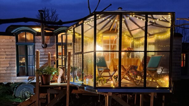 A glass greenhouse structure with a wooden deck, potted plants, and a chair. - Tiny house # starry view # sauna # wild hot (Carinerland)