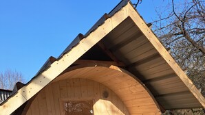 A wooden cylindrical structure with a pitched roof, a bench, and a small table. - Tiny house # starry view # sauna # wild hot (Carinerland)