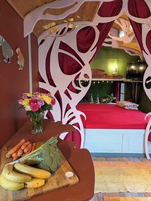 Ein Zimmer mit einem Bett, einem Holztisch mit Obst und Gemüse, einer Blumenvase und einem Fernseher.