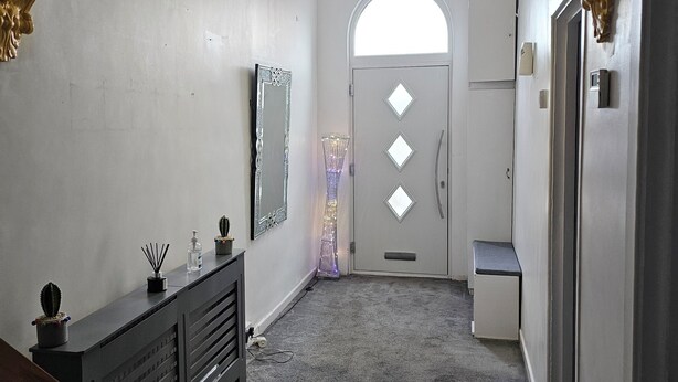 Un couloir orné d’un lustre, une porte avec des motifs découpés en forme de losanges et un miroir accroché au mur.