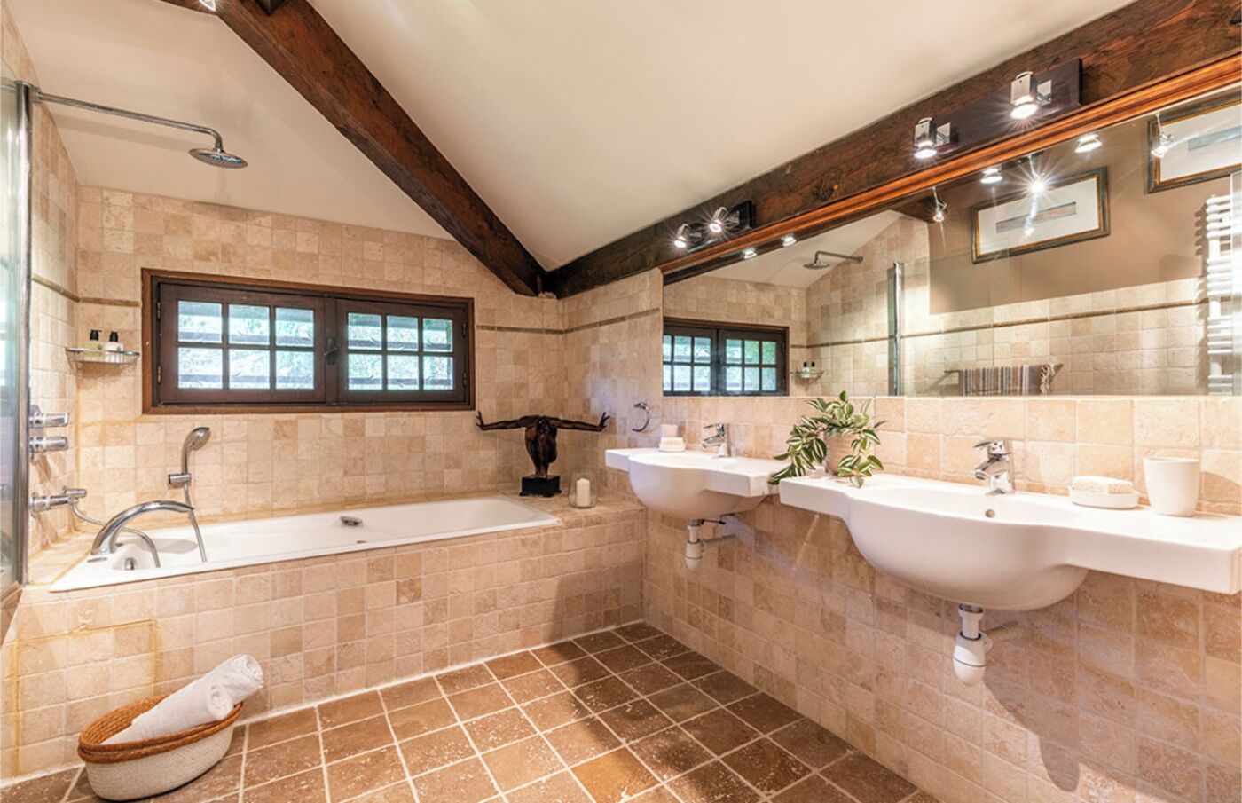 A modern bathroom with a bathtub, two sinks, a large mirror, and a window.